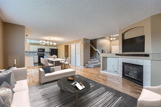 5130 S Wenatchee St, Aurora, CO 80015 - living area with a textured ceiling, light wood-type flooring, a fireplace, a chandelier, and stairs