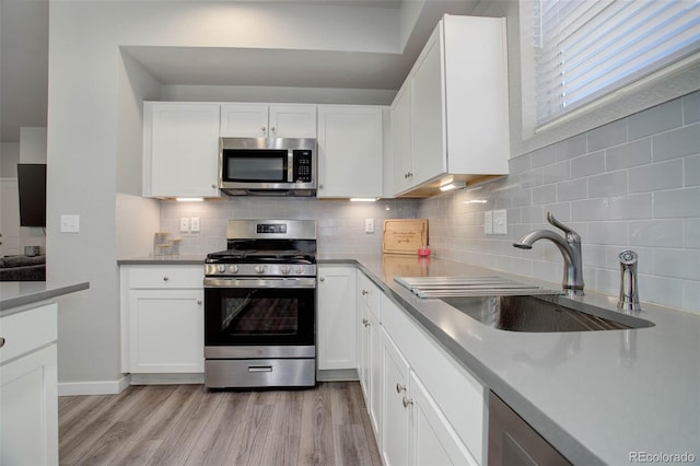 kitchen featuring appliances with stainless steel finishes, sink, white cabinets, backsplash, and light hardwood / wood-style flooring