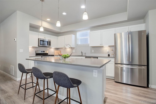 kitchen featuring decorative light fixtures, stainless steel appliances, white cabinets, and a kitchen island