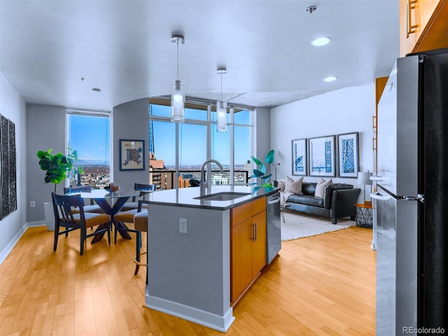 kitchen featuring sink, a center island with sink, light hardwood / wood-style flooring, a wall of windows, and stainless steel appliances