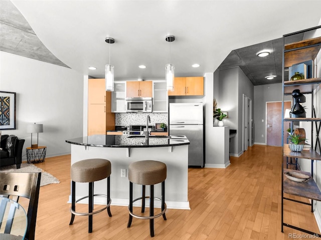 kitchen with hanging light fixtures, stainless steel appliances, a kitchen bar, light brown cabinetry, and light wood-type flooring