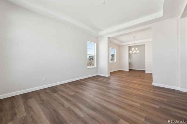 spare room with dark wood-style flooring, baseboards, an inviting chandelier, and a raised ceiling