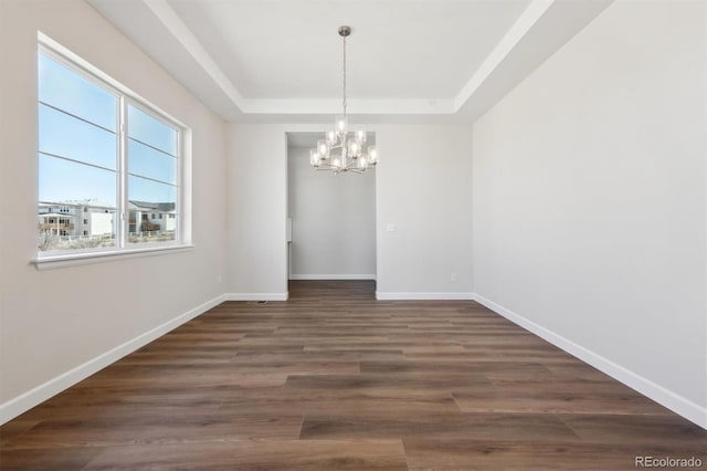 unfurnished dining area with baseboards, a tray ceiling, an inviting chandelier, and wood finished floors