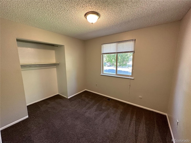 unfurnished bedroom with a textured ceiling, dark colored carpet, and a closet