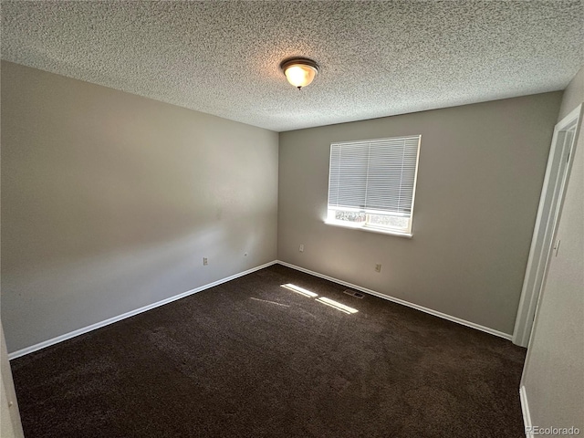 spare room with a textured ceiling and dark carpet