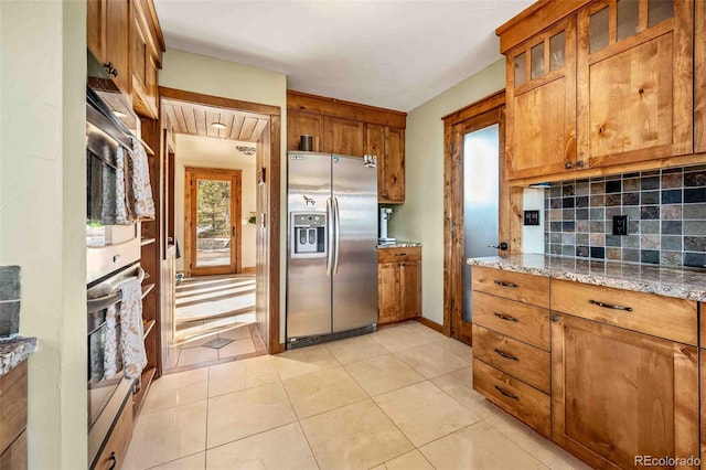 kitchen featuring decorative backsplash, stainless steel fridge with ice dispenser, light tile patterned floors, and light stone counters