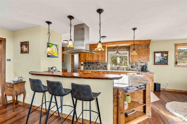 kitchen featuring hanging light fixtures, dark wood-type flooring, tasteful backsplash, island exhaust hood, and kitchen peninsula