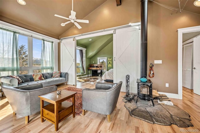 sunroom / solarium featuring a barn door, ceiling fan, vaulted ceiling, and a wood stove