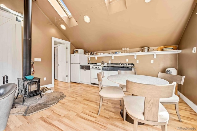 dining area featuring lofted ceiling with skylight, a wood stove, and light hardwood / wood-style flooring