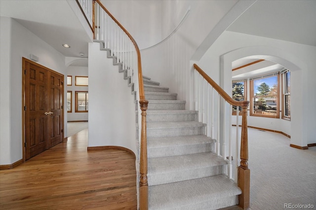 stairway with baseboards, arched walkways, wood finished floors, and recessed lighting