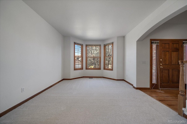 unfurnished room with arched walkways, light carpet, and baseboards