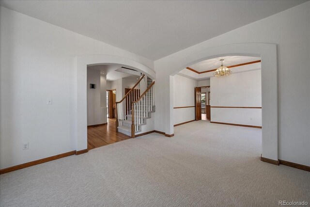 carpeted empty room featuring ornamental molding, arched walkways, stairway, and baseboards