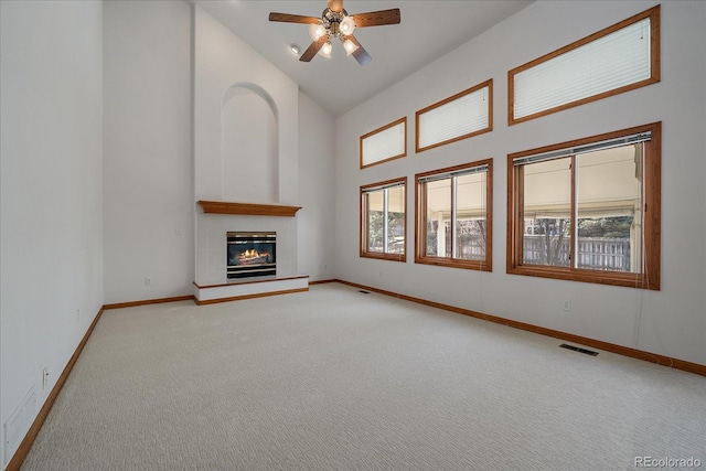 unfurnished living room with baseboards, visible vents, a glass covered fireplace, carpet flooring, and high vaulted ceiling