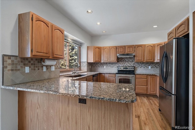 kitchen featuring under cabinet range hood, a peninsula, a sink, appliances with stainless steel finishes, and light wood-type flooring