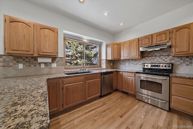 kitchen featuring stainless steel appliances, light wood-style flooring, a sink, light stone countertops, and under cabinet range hood