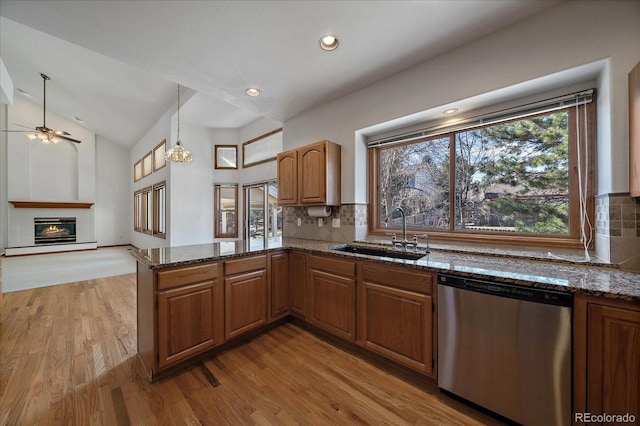 kitchen featuring a glass covered fireplace, lofted ceiling, a peninsula, stainless steel dishwasher, and a sink