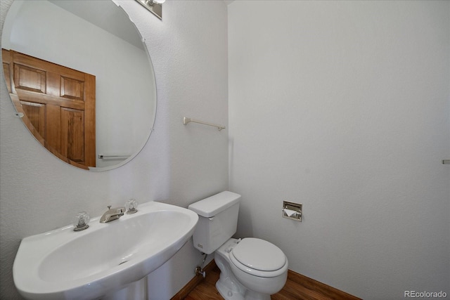 half bathroom featuring wood finished floors, a sink, toilet, and baseboards