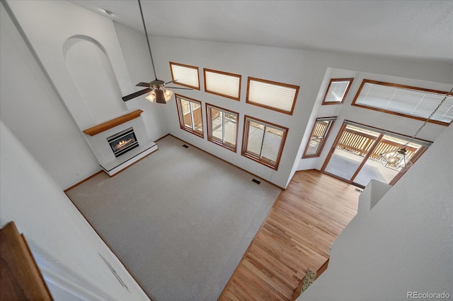 living room featuring visible vents, a ceiling fan, a glass covered fireplace, wood finished floors, and high vaulted ceiling