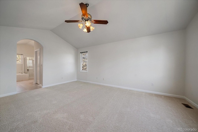 spare room with arched walkways, light colored carpet, visible vents, vaulted ceiling, and baseboards