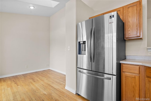 kitchen featuring stainless steel fridge with ice dispenser, light wood-type flooring, and a skylight