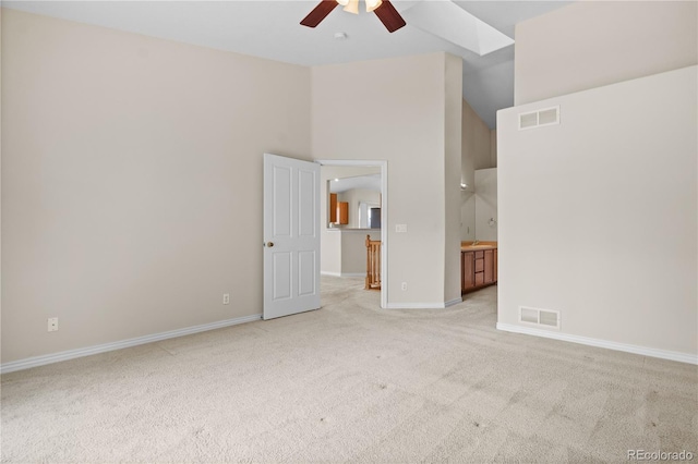 empty room with ceiling fan, a high ceiling, light colored carpet, and a skylight