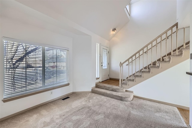 foyer featuring visible vents, carpet, baseboards, stairway, and high vaulted ceiling