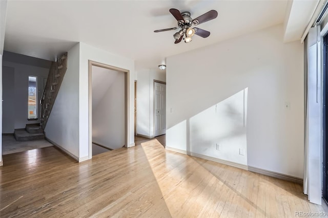 unfurnished living room featuring a ceiling fan, stairs, baseboards, and wood finished floors