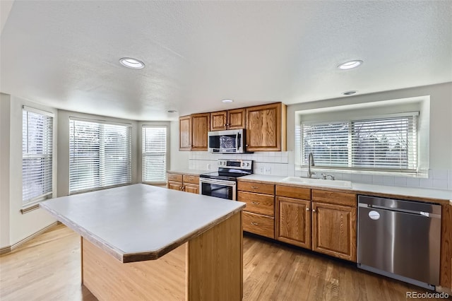 kitchen featuring brown cabinets, light wood-style flooring, a sink, backsplash, and appliances with stainless steel finishes