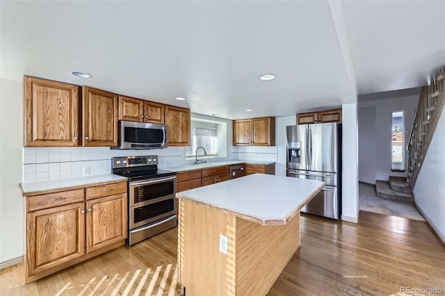 kitchen featuring light wood finished floors, a sink, backsplash, stainless steel appliances, and light countertops