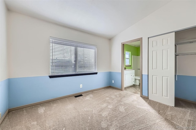 unfurnished bedroom featuring visible vents, connected bathroom, vaulted ceiling, carpet flooring, and a closet