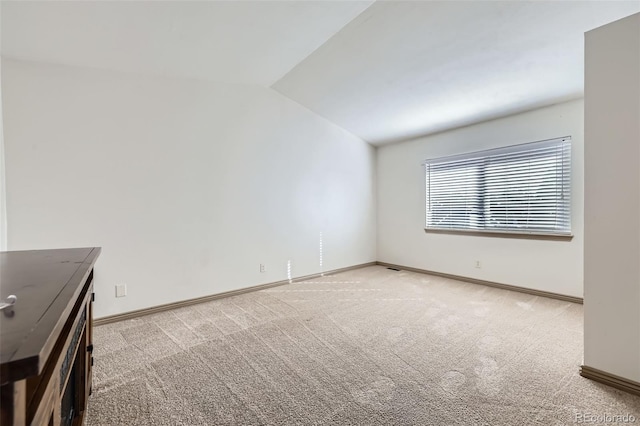 spare room featuring lofted ceiling, carpet, and baseboards