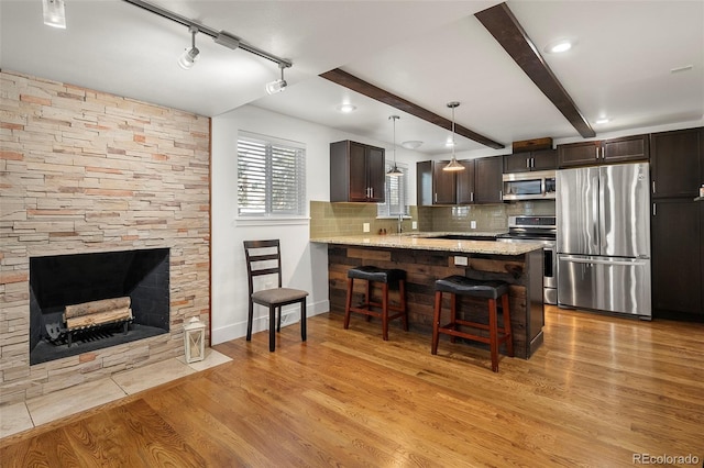 kitchen featuring backsplash, kitchen peninsula, light hardwood / wood-style floors, a breakfast bar, and appliances with stainless steel finishes