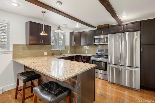 kitchen with a kitchen breakfast bar, kitchen peninsula, appliances with stainless steel finishes, beam ceiling, and dark brown cabinetry