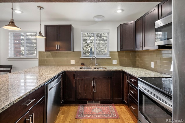 kitchen featuring backsplash, sink, hanging light fixtures, light hardwood / wood-style floors, and stainless steel appliances