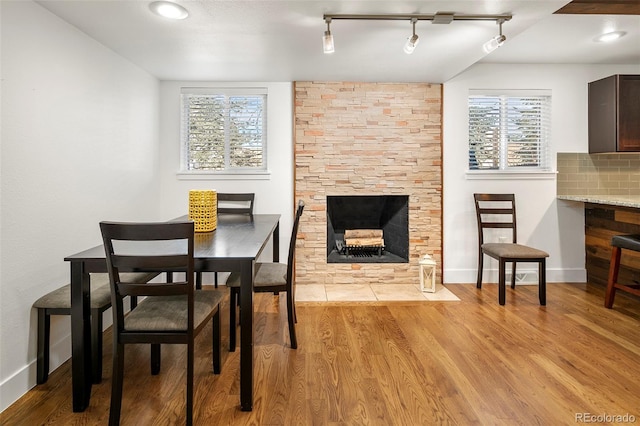 dining area featuring a stone fireplace, track lighting, and light wood-type flooring