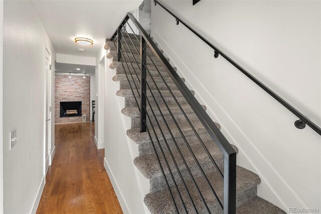 staircase featuring wood-type flooring and a stone fireplace