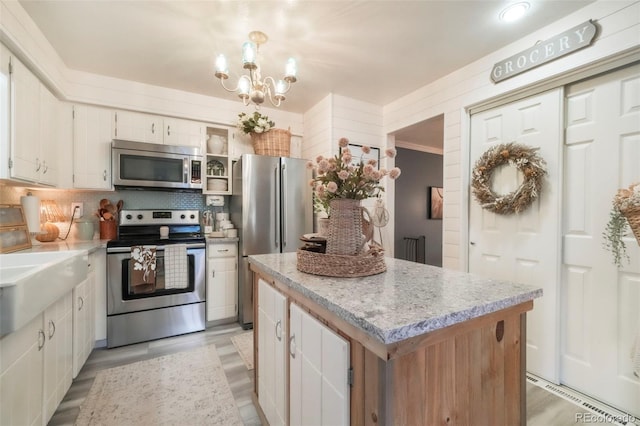 8280 Everett Way, Arvada, CO 80005 - kitchen with appliances with stainless steel finishes, a kitchen island, a chandelier, tasteful backsplash, and white cabinets