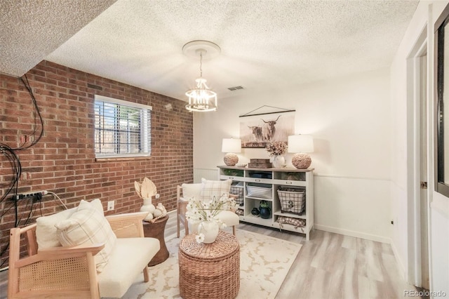 8280 Everett Way, Arvada, CO 80005 - sitting room featuring wood finished floors, brick wall, a chandelier, and a textured ceiling