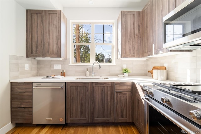 kitchen with stainless steel appliances, tasteful backsplash, sink, and light wood-type flooring