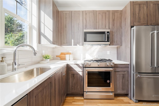 kitchen with stainless steel appliances, sink, backsplash, and light wood-type flooring