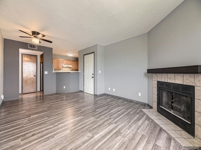 unfurnished living room with light wood-style flooring, a tile fireplace, and baseboards