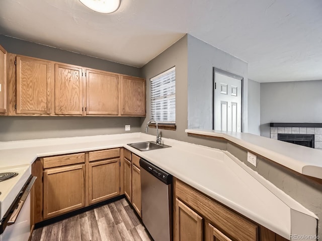 kitchen featuring stainless steel dishwasher, a sink, stove, wood finished floors, and light countertops