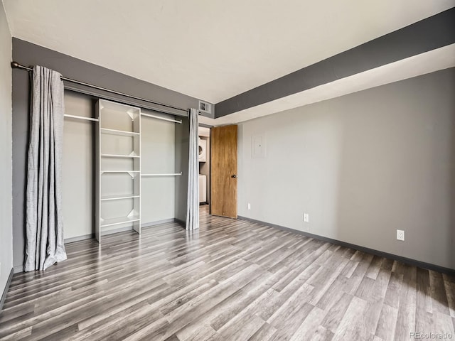 unfurnished bedroom with wood finished floors, baseboards, and a closet