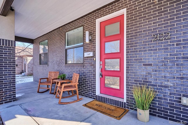 doorway to property with covered porch and brick siding