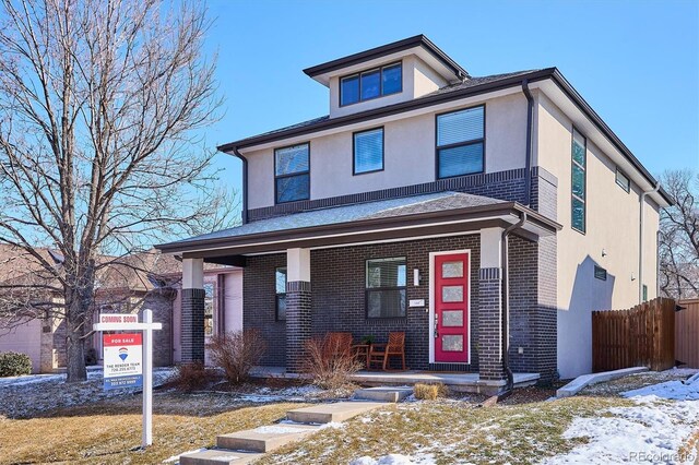 american foursquare style home with covered porch, fence, stucco siding, and brick siding