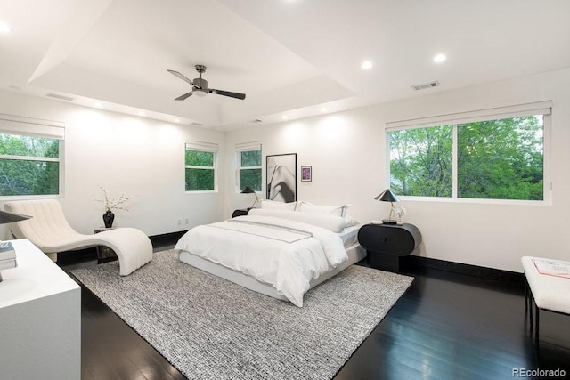 bedroom with a tray ceiling, multiple windows, dark wood-style floors, recessed lighting, and baseboards