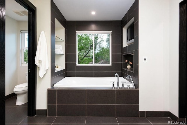 full bath featuring toilet, a garden tub, tile patterned flooring, and baseboards