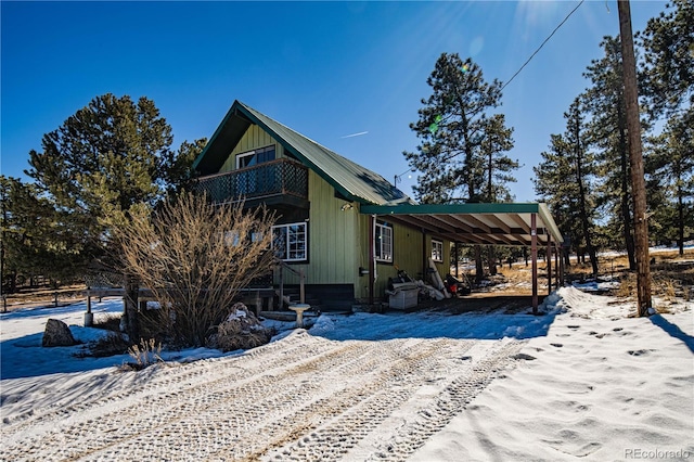 view of snowy exterior featuring an attached carport, driveway, and a balcony