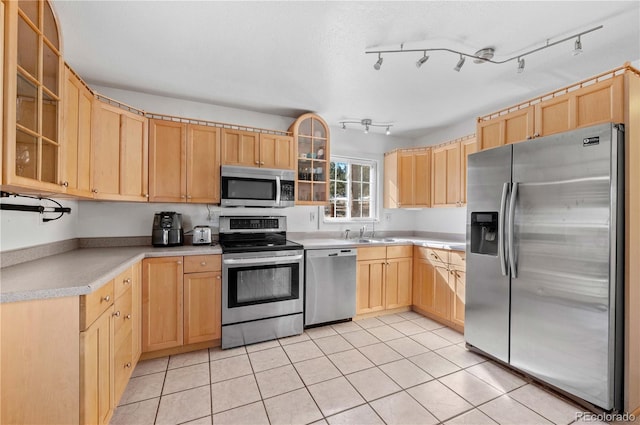 kitchen with light brown cabinetry, appliances with stainless steel finishes, light countertops, light tile patterned floors, and glass insert cabinets