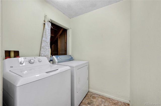 washroom with stone finish floor, washer and dryer, a textured ceiling, baseboards, and laundry area